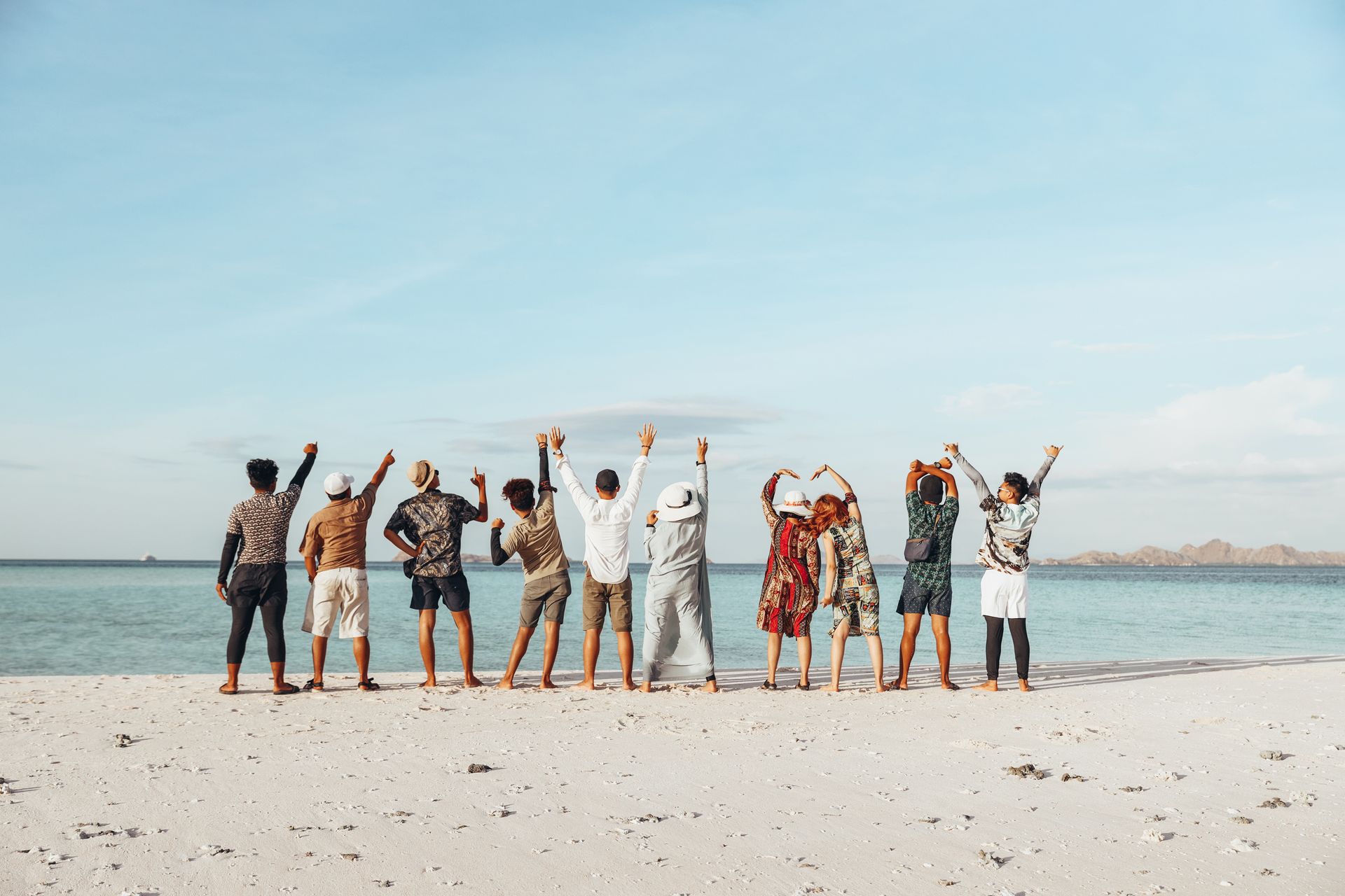 Group of people on a beach, smiling and raising their arms under a blue sky.