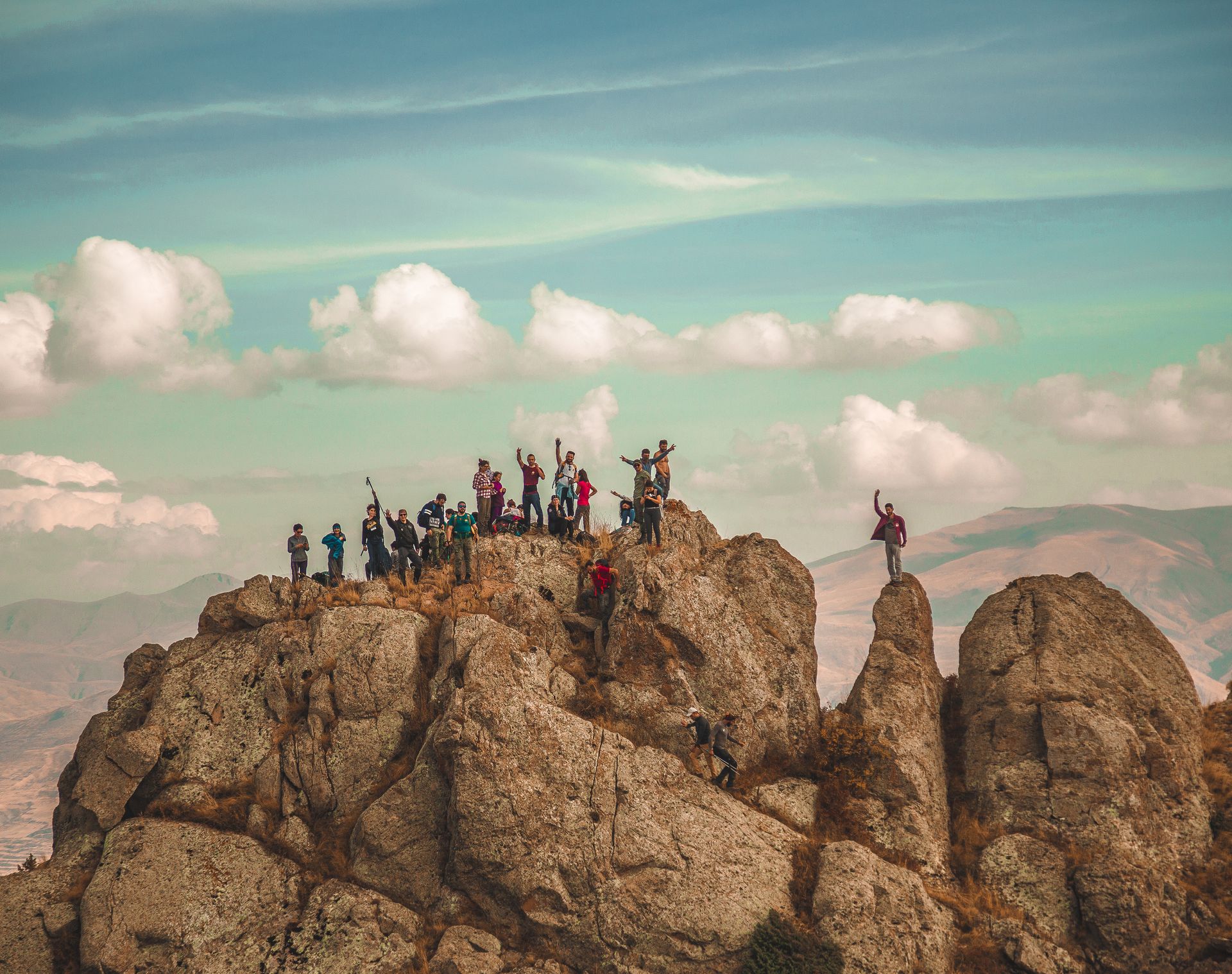 Hikers standing on rocky mountain peaks under a blue sky with scattered clouds