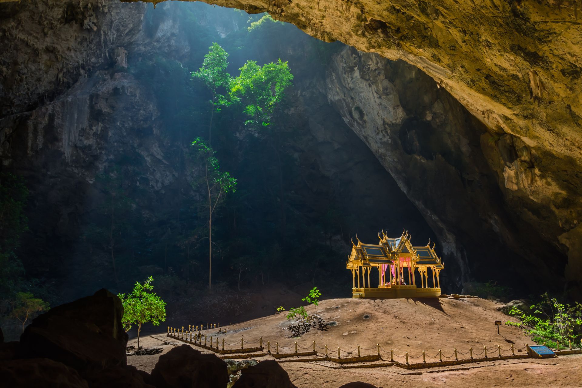 Small ornate shrine inside a rocky cave with sunlight and green plants filtering in from above