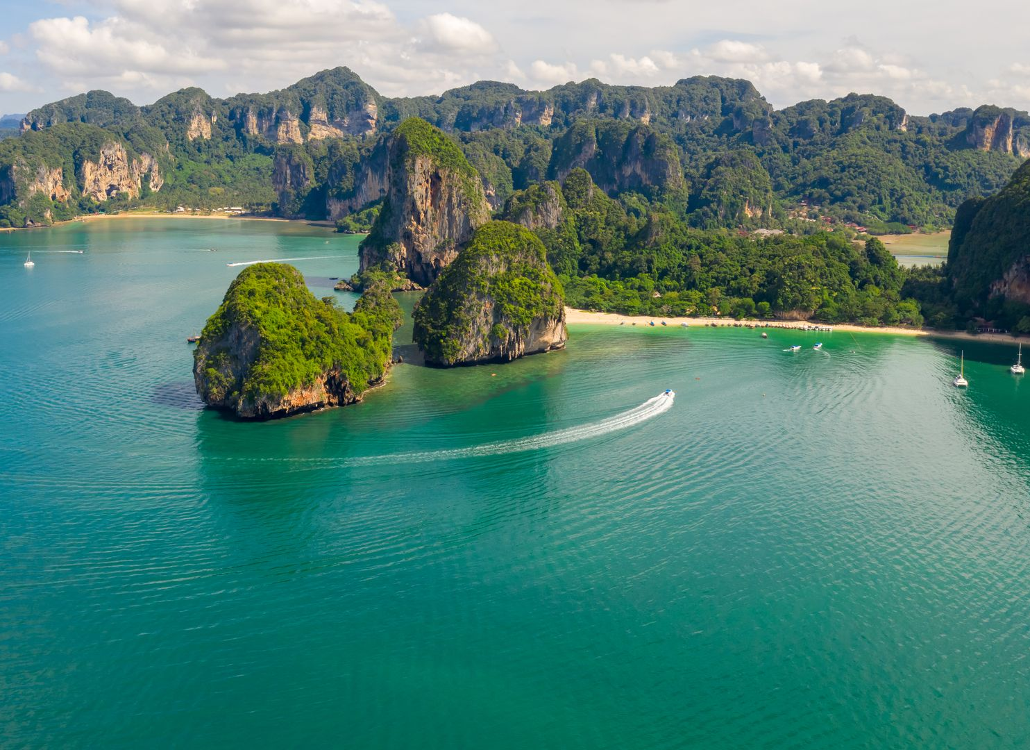 Limestone islands and turquoise water with a speedboat leaving a white wake in a tropical bay