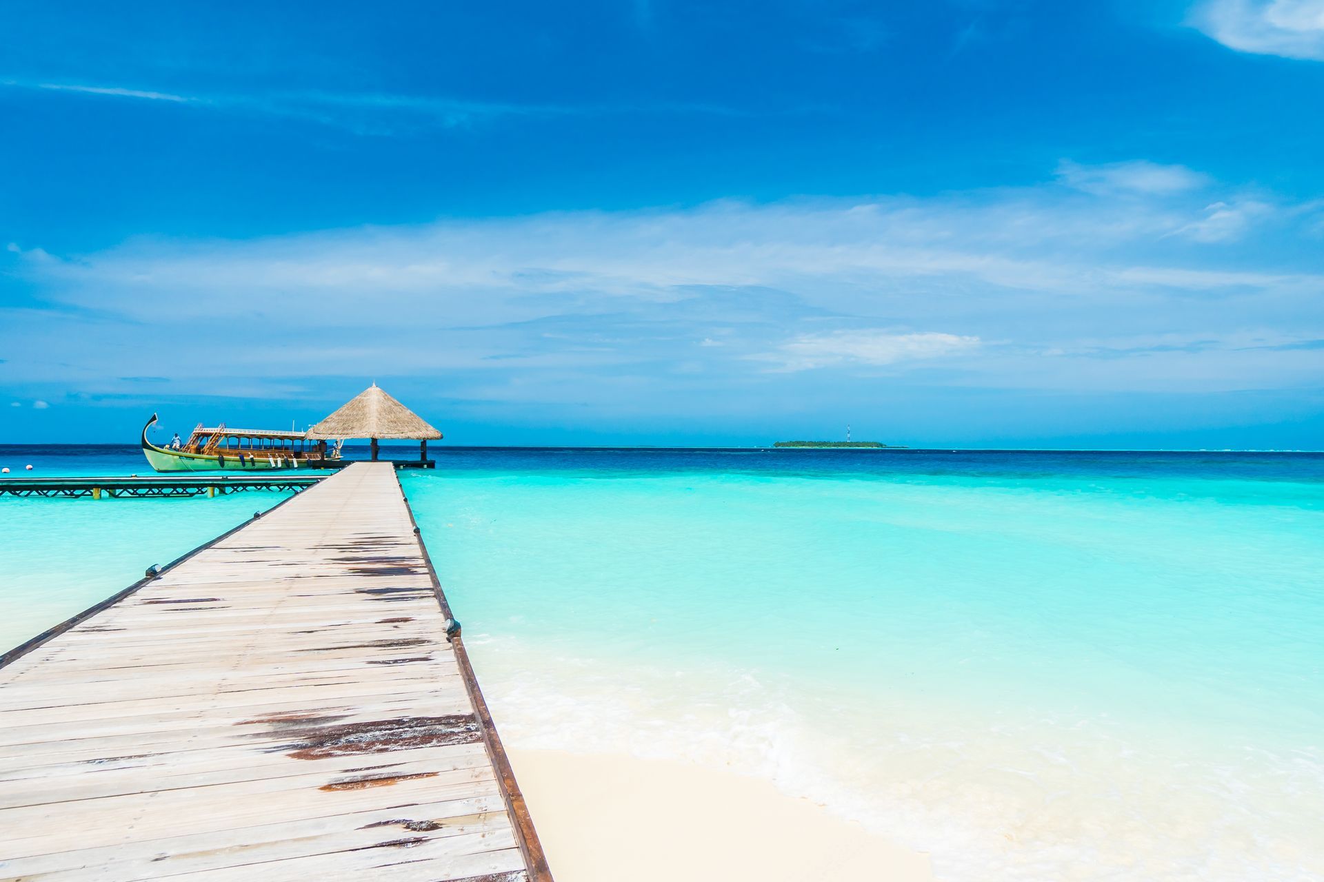 Wooden pier leading to a thatched hut over a turquoise tropical sea under a bright blue sky