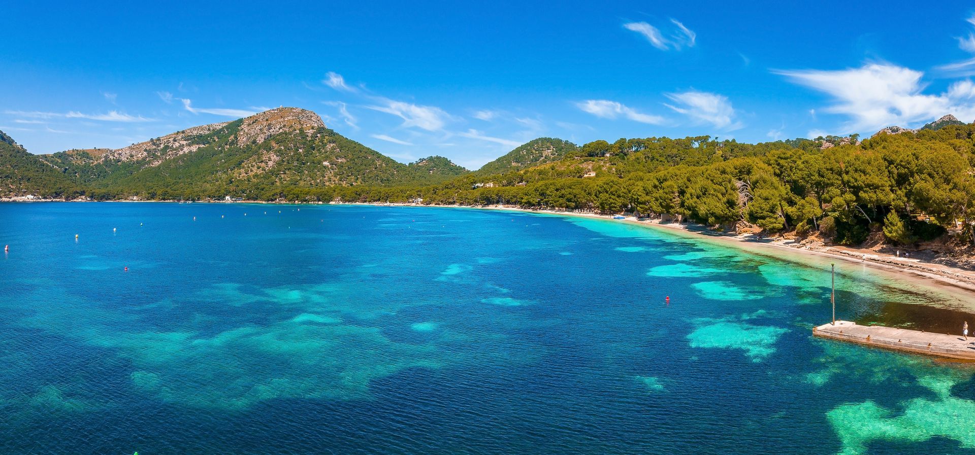 Tropical bay with turquoise water, sandy beach, palm trees, and a rocky hill under a blue sky