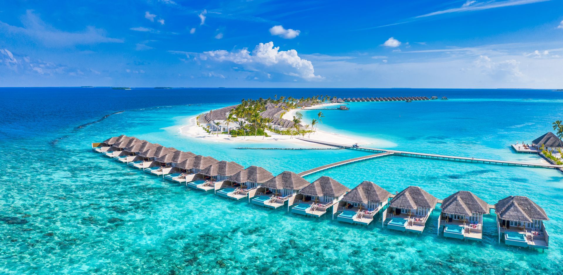 Aerial view of turquoise lagoon with overwater bungalows and a small tropical island under a blue sky