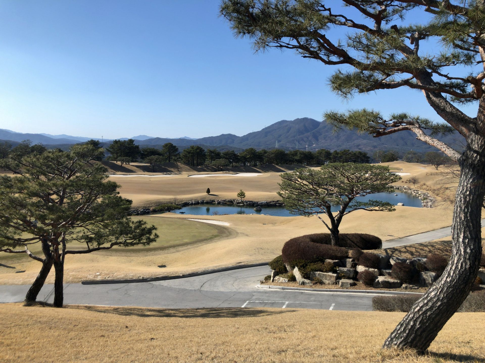 Golf course landscape with sand traps, water hazard, trees, and mountains in the distance