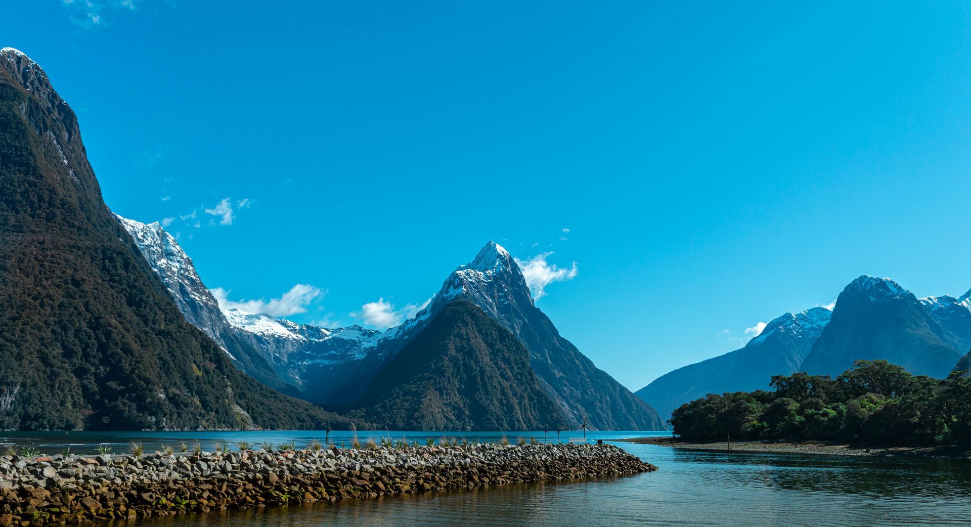 Rocky mountain peaks beside a calm river under a bright blue sky