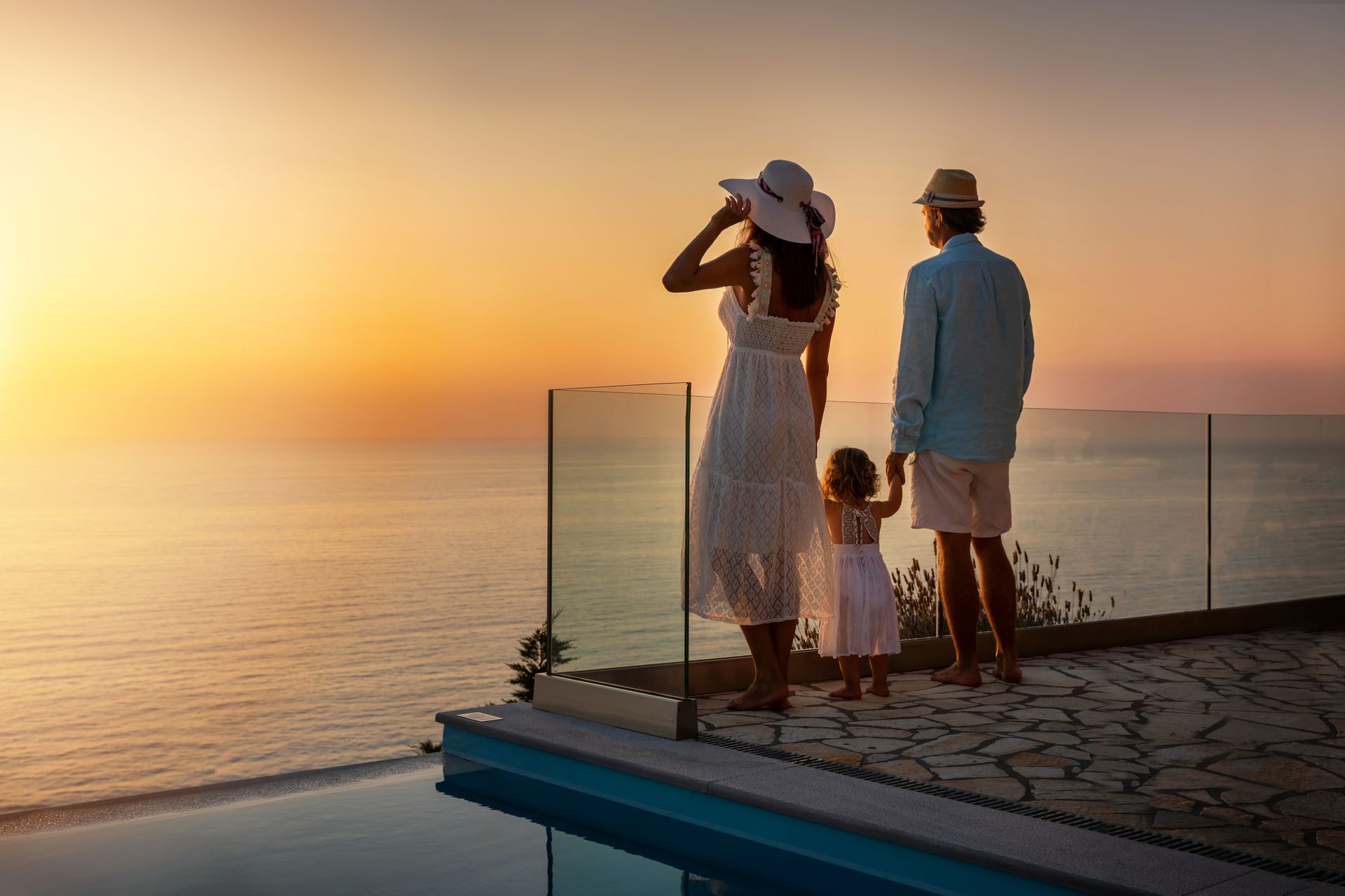 Family standing on a seaside deck at sunset, looking out over calm water.