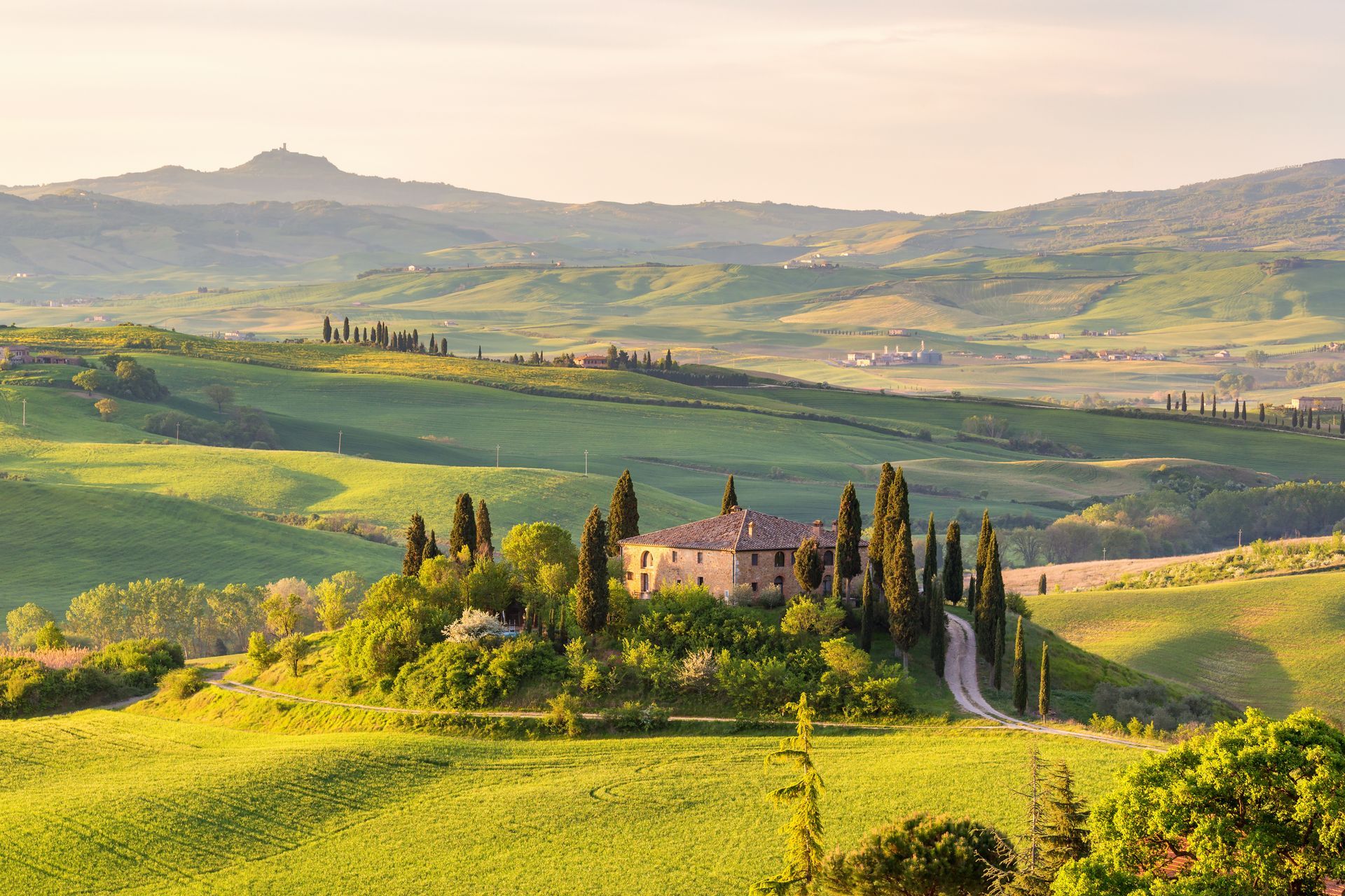 Sunlit Tuscan countryside with rolling green hills and a villa surrounded by cypress trees