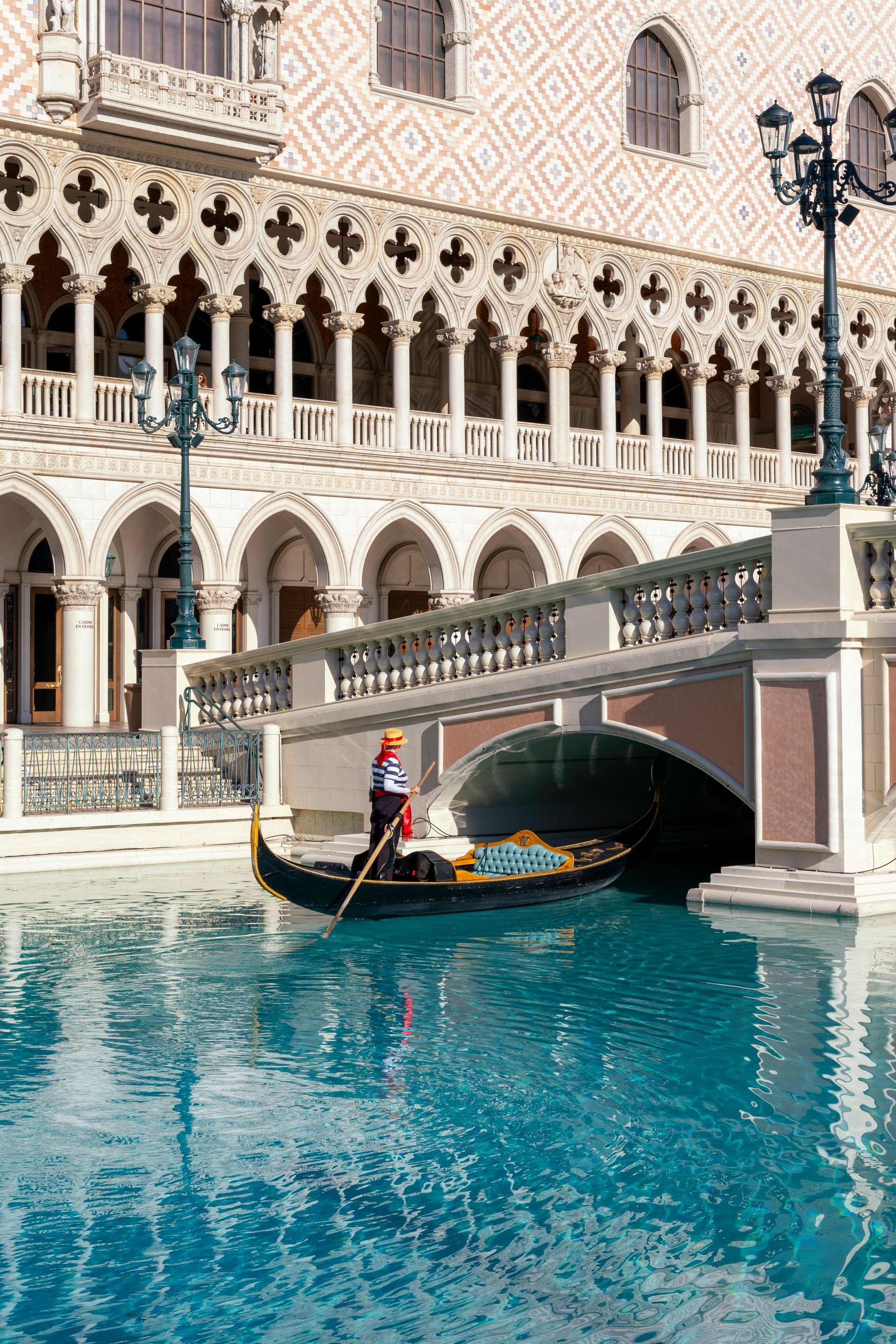 Gondola passing under a bridge on a turquoise canal beside ornate Venetian-style buildings