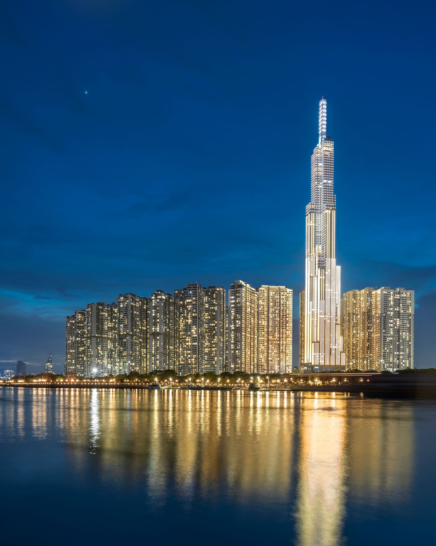 Nighttime city skyline with a brightly lit tall skyscraper reflected in calm water