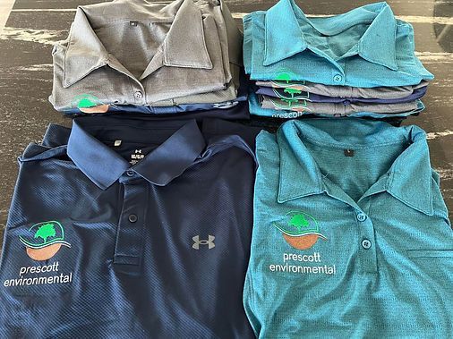 Four stacks of polo shirts in various shades of blue and gray, with a company logo embroidered on the front.