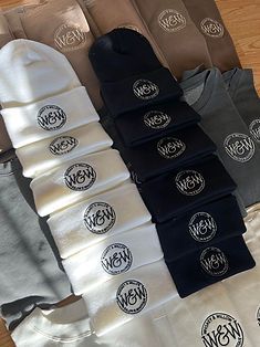 Stacks of beanies and sweatshirts in various neutral colors, all with an embroidered 