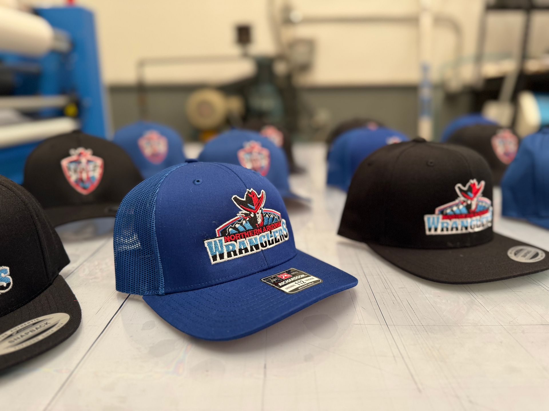 Blue and black Warriors team hats with logo, sitting on a table in a workshop setting.