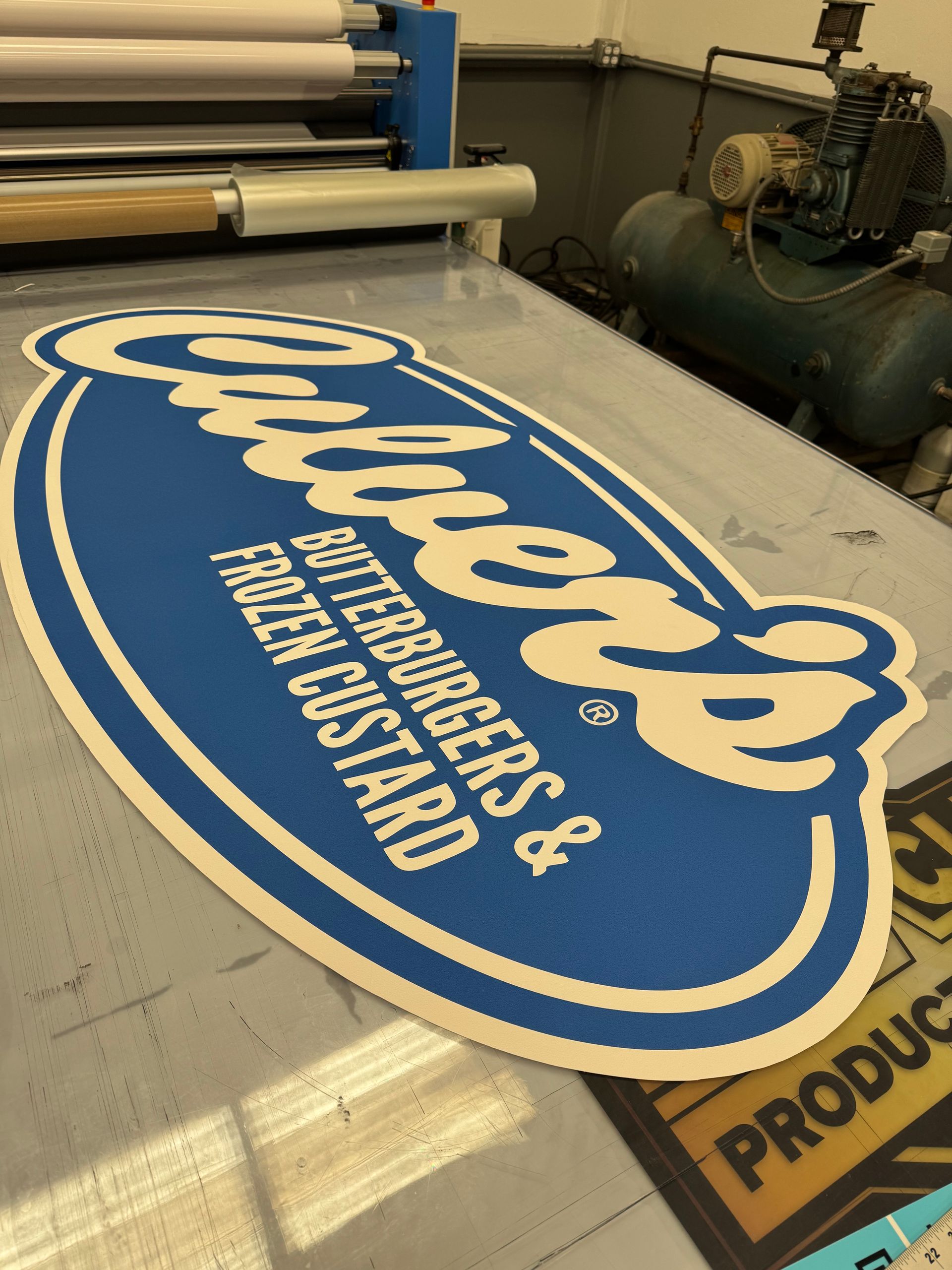 Close-up of a printed Culver's sign on a table, with a laminating machine in the background.