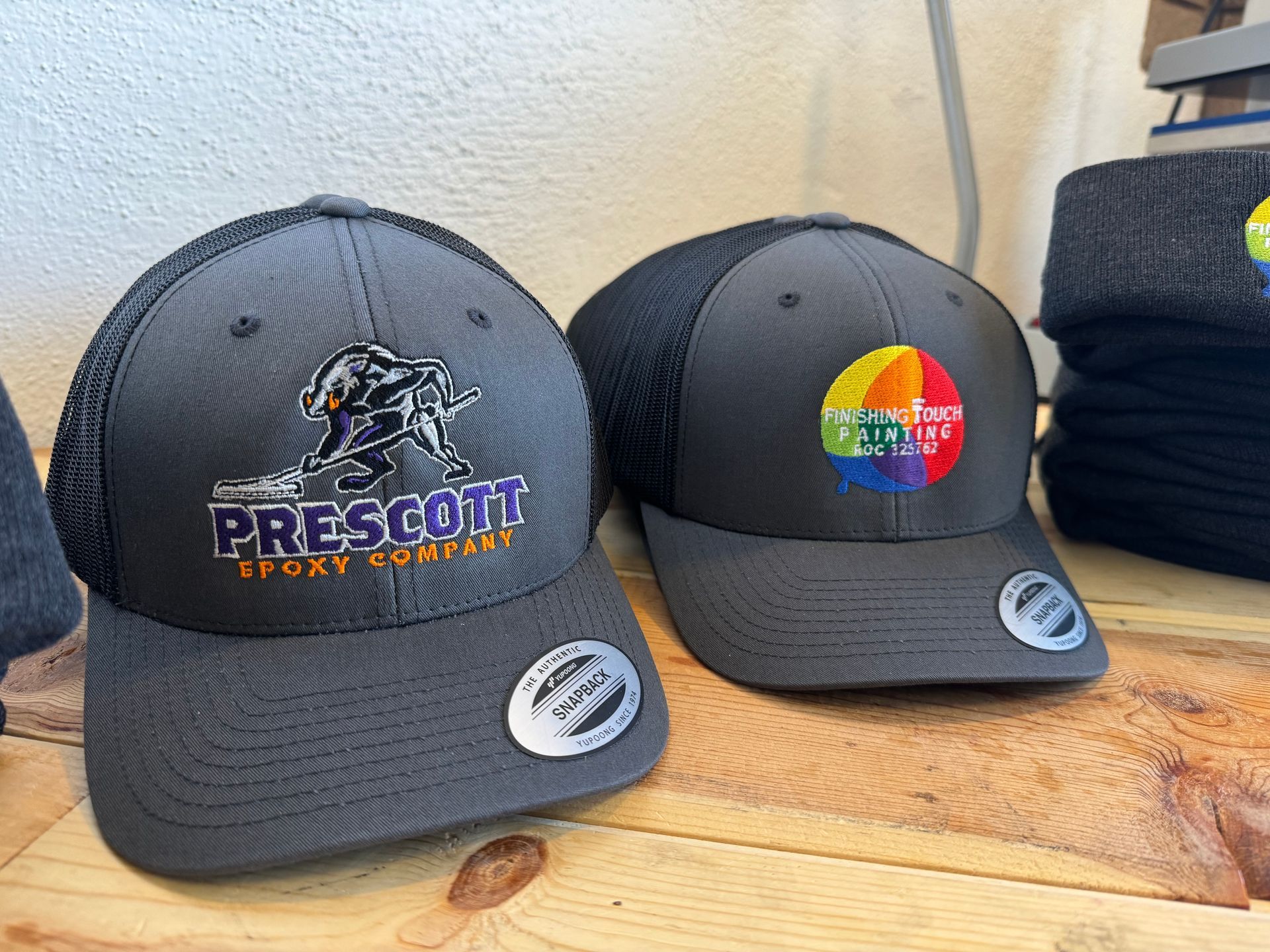 Two gray Prescott Sport Company hats on display. One has a logo of a person wrestling, the other a colorful circle design.