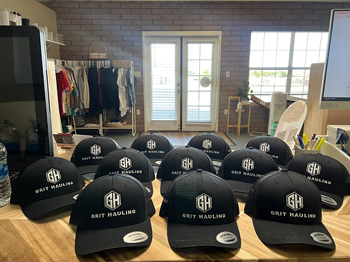 Black hats with white logos on a wooden table. A brick wall and window in the background.