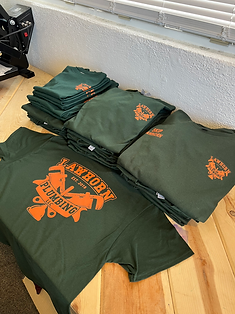 Green t-shirts with orange logos stacked on a wooden surface. 
