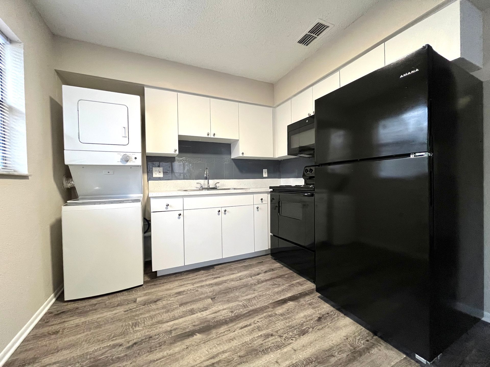 Small kitchen with black appliances and white cabinets. Washer and dryer stack beside the window.