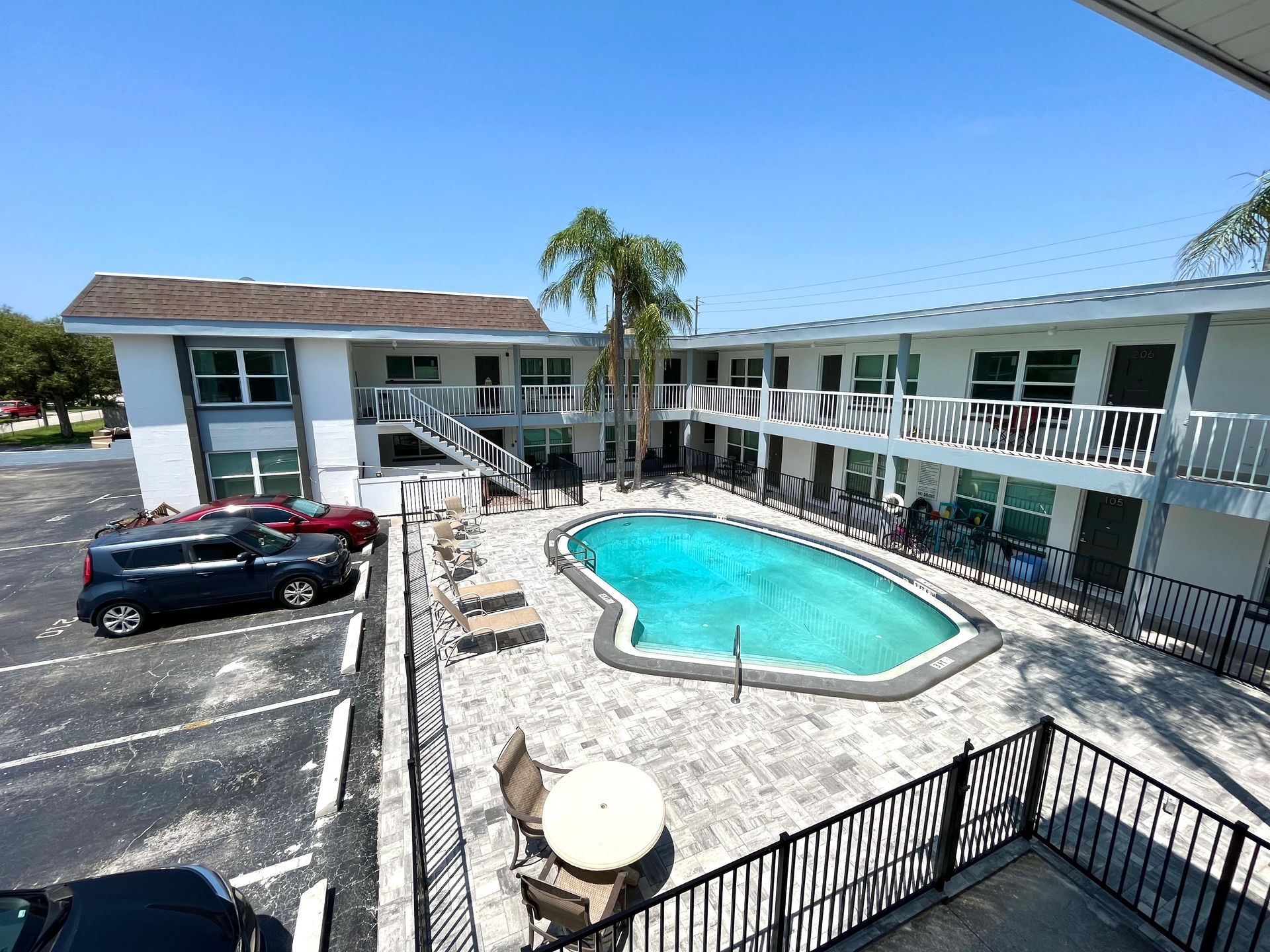 Apartment complex with a pool and parking area, clear sky.