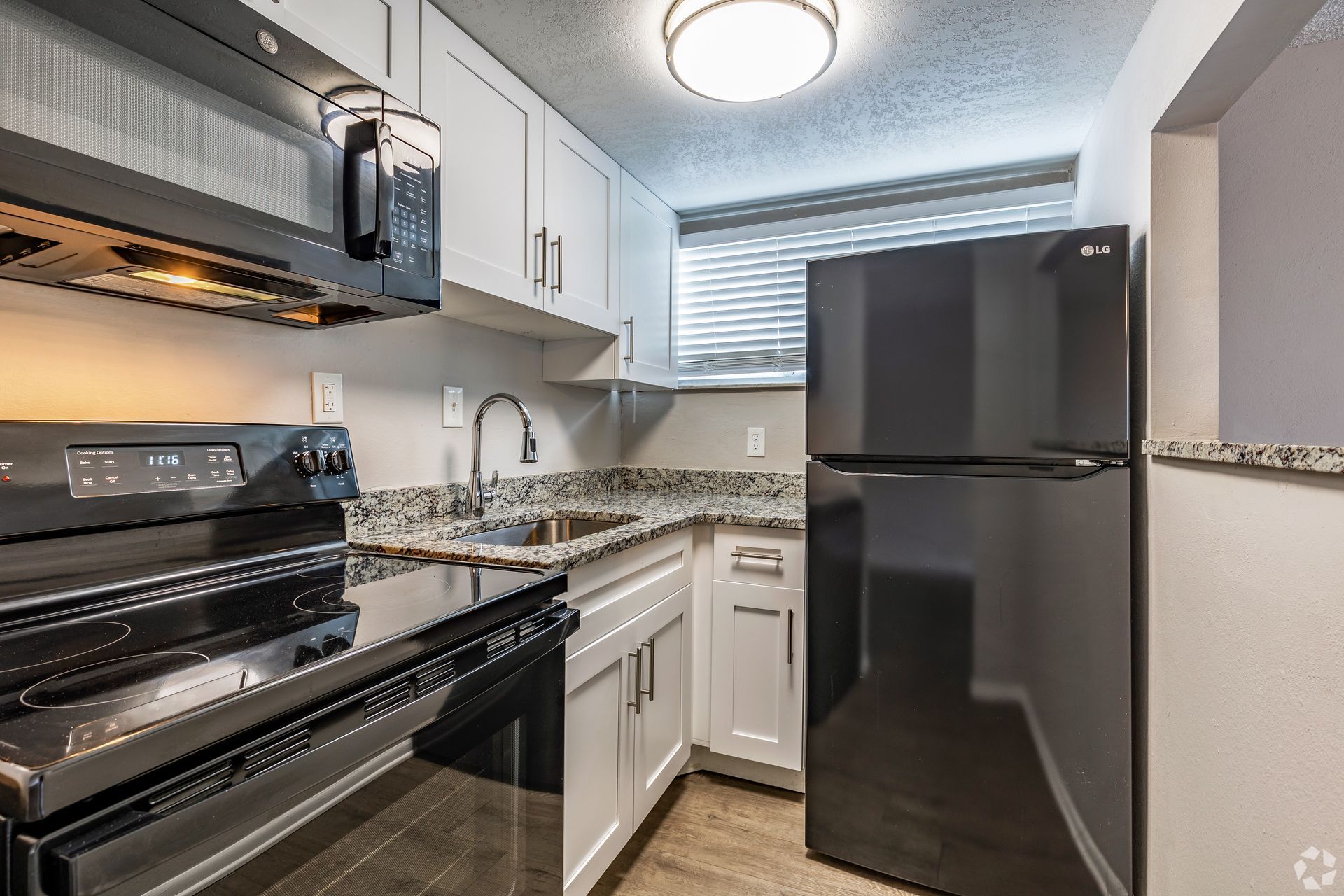 Small, modern kitchen with white cabinets, black appliances, and granite countertops.