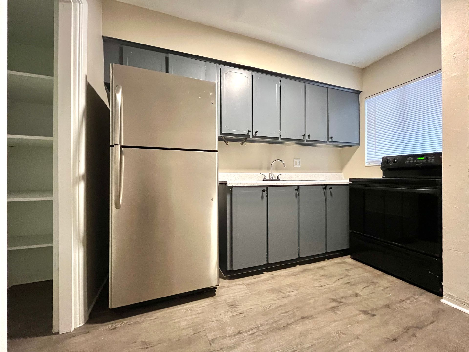 Kitchen with gray cabinets, stainless steel refrigerator, and black stove.