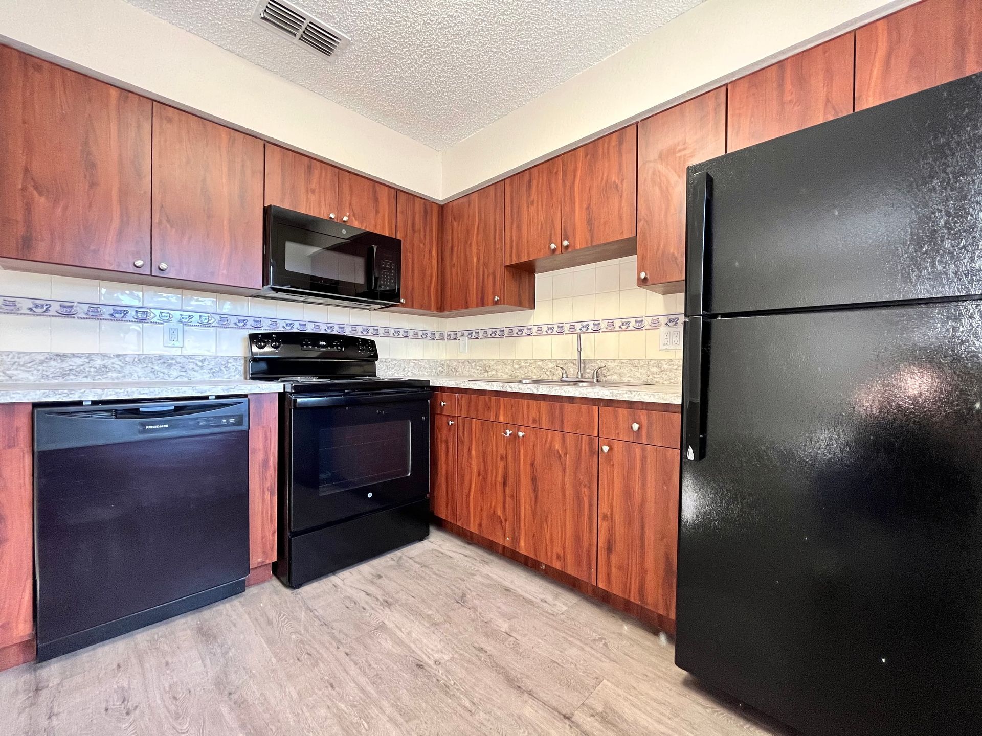 Black appliances in a white kitchen with white cabinets and light wood-look flooring.