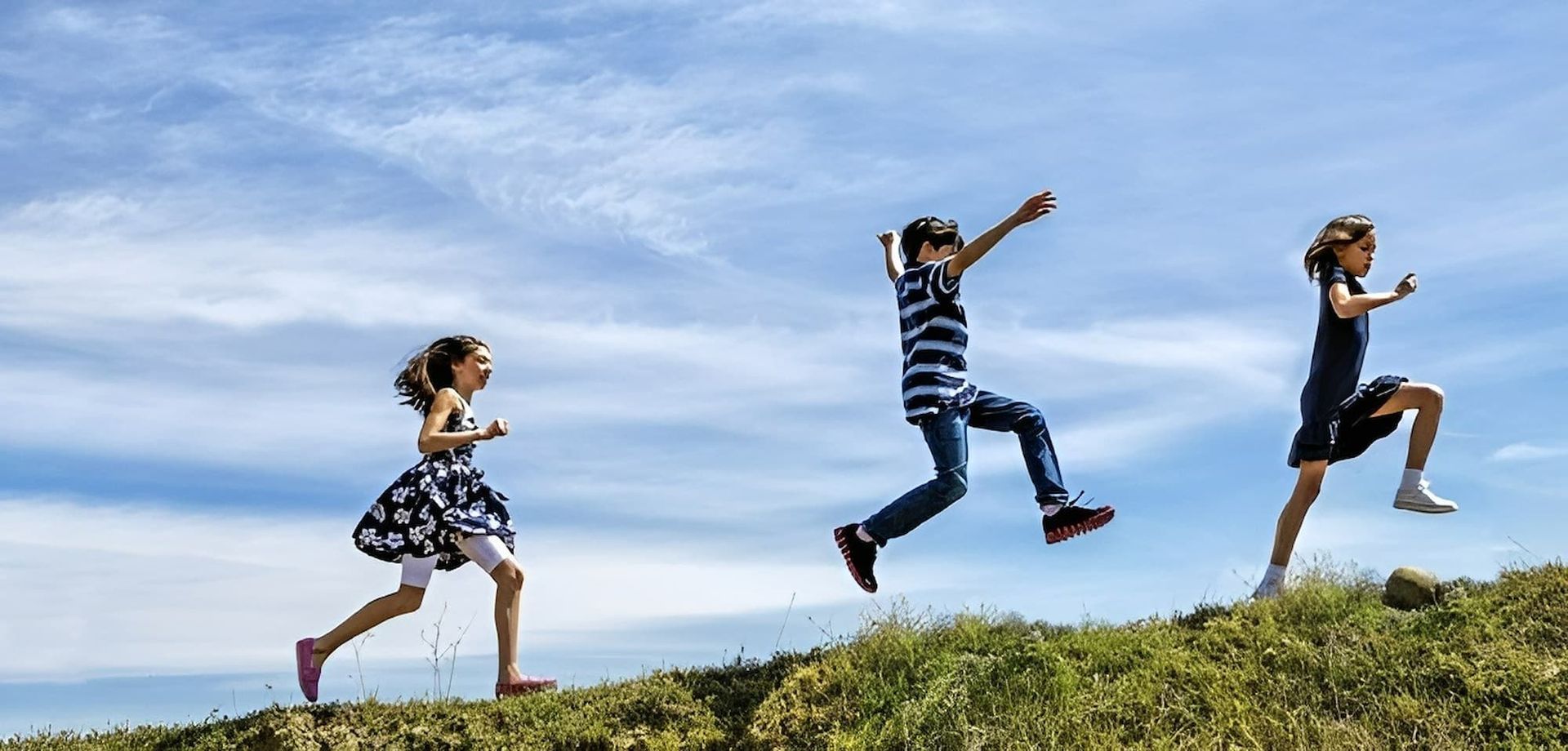 Three Children Are Jumping in The Air on Top of A Grassy Hill — Psych Solutions NT in Alice Spring, NT
