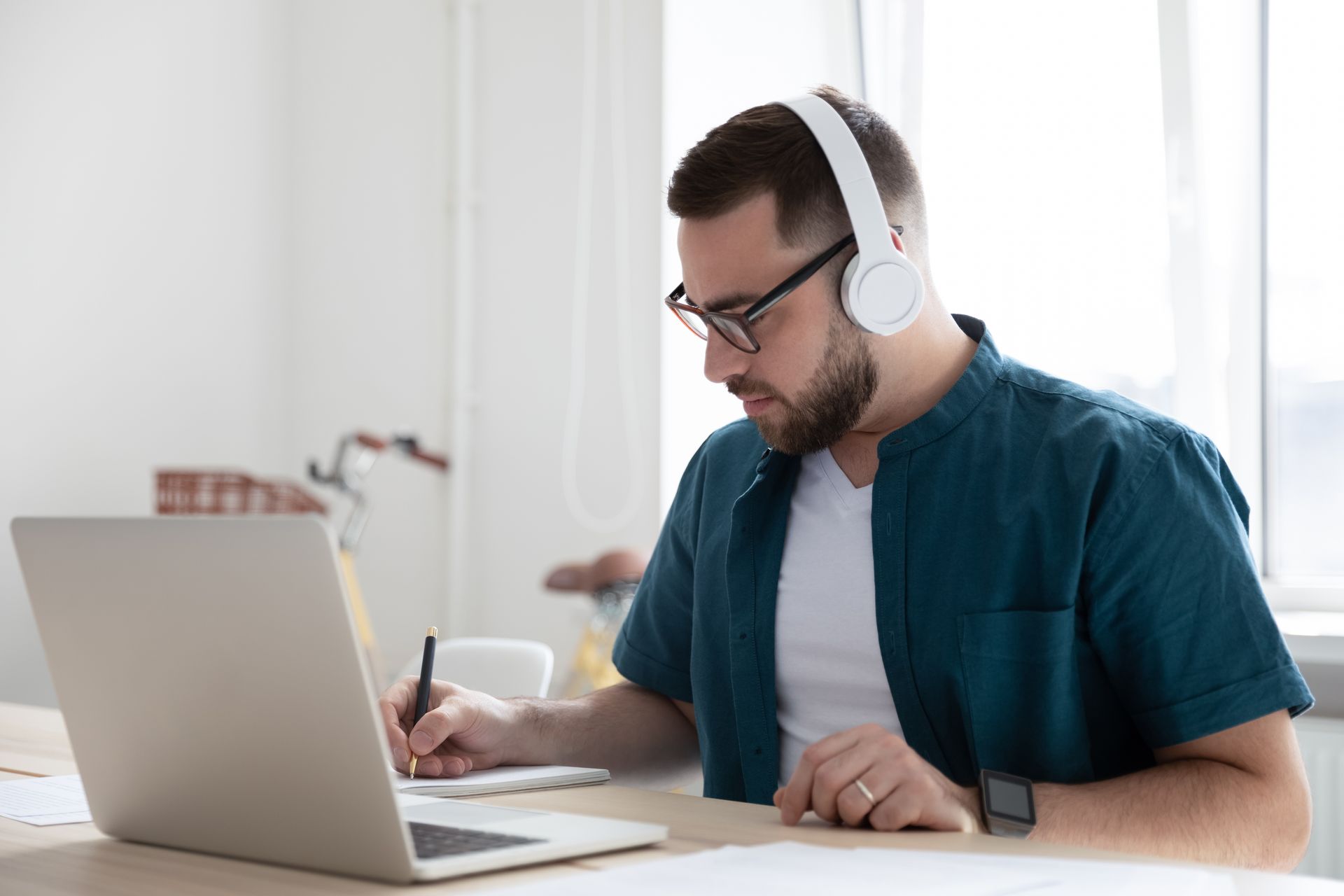 A man wearing headphones is sitting at a desk using a laptop computer. — Psych Solutions NT in Leanyer, NT