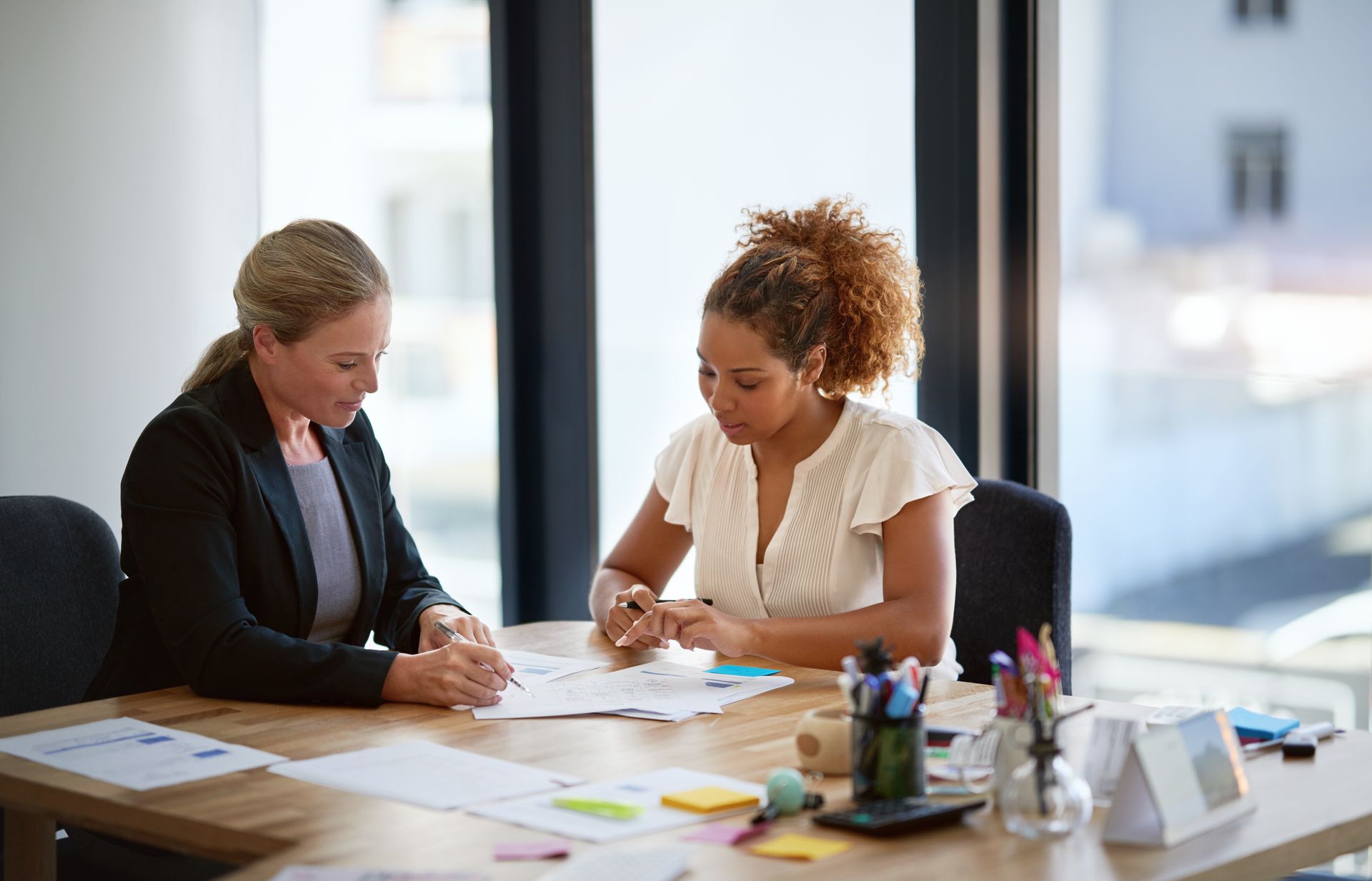 Two women are sitting at a table looking at papers. — Psych Solutions NT in Leanyer, NT