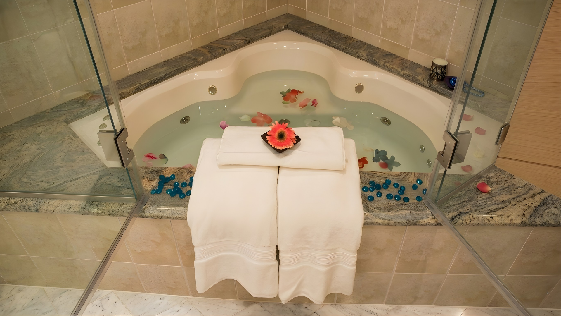 Spa bathtub with scattered flower petals and a white towel-covered tray holding candles and a red flower arrangement.