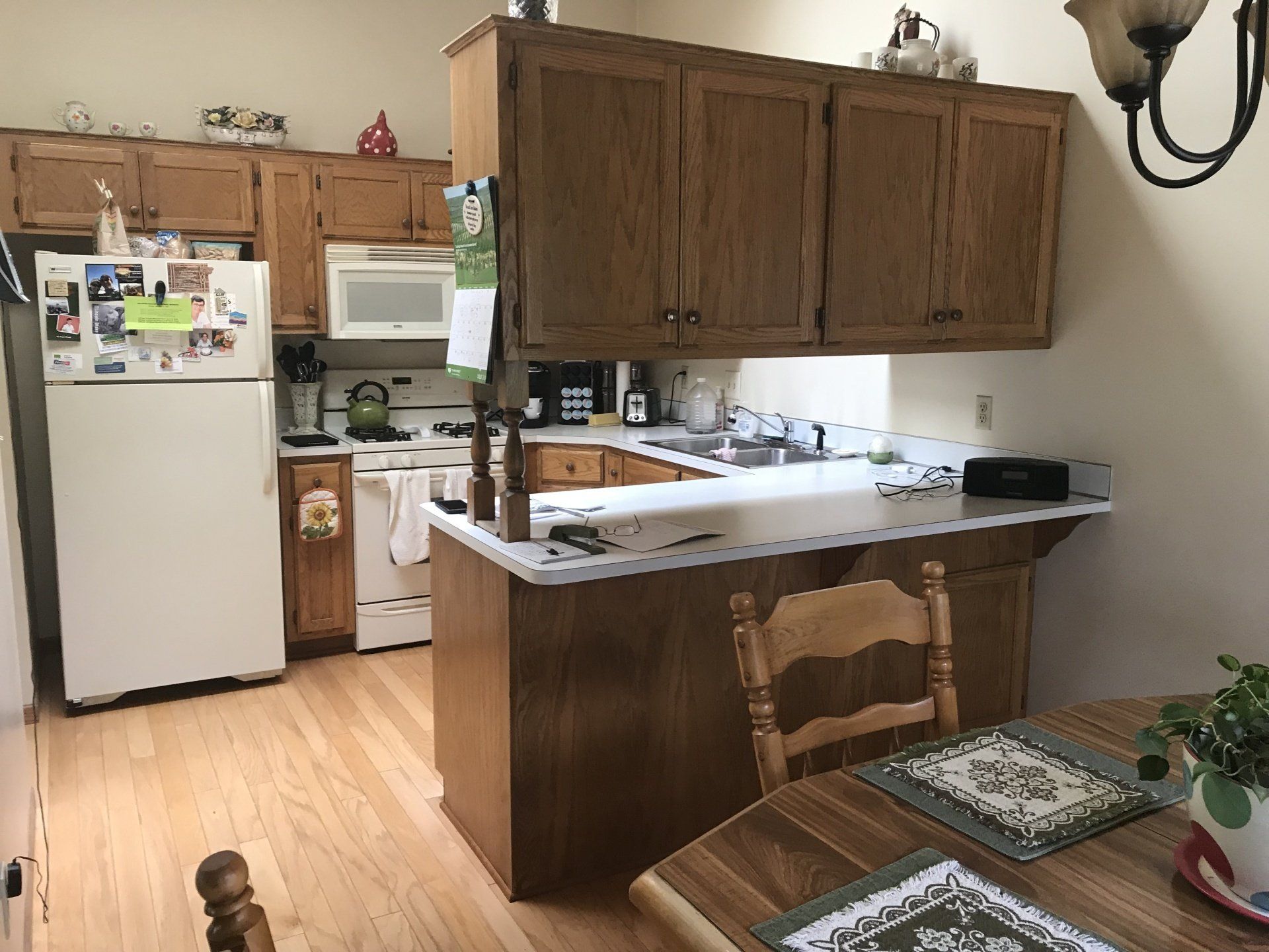 Kitchen with wood cabinets, white appliances, light countertops, and a wooden table.
