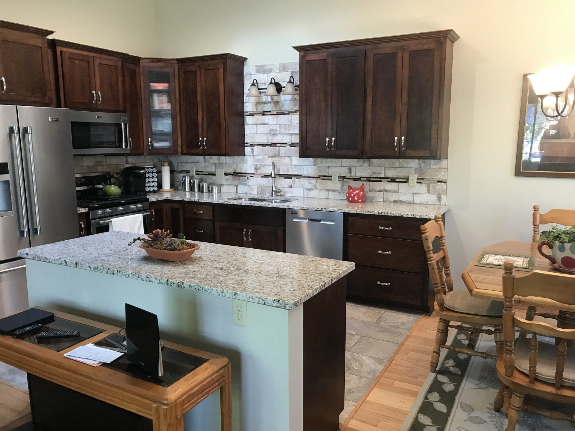 Kitchen with dark cabinets, granite counters, stainless steel appliances and a dining table.