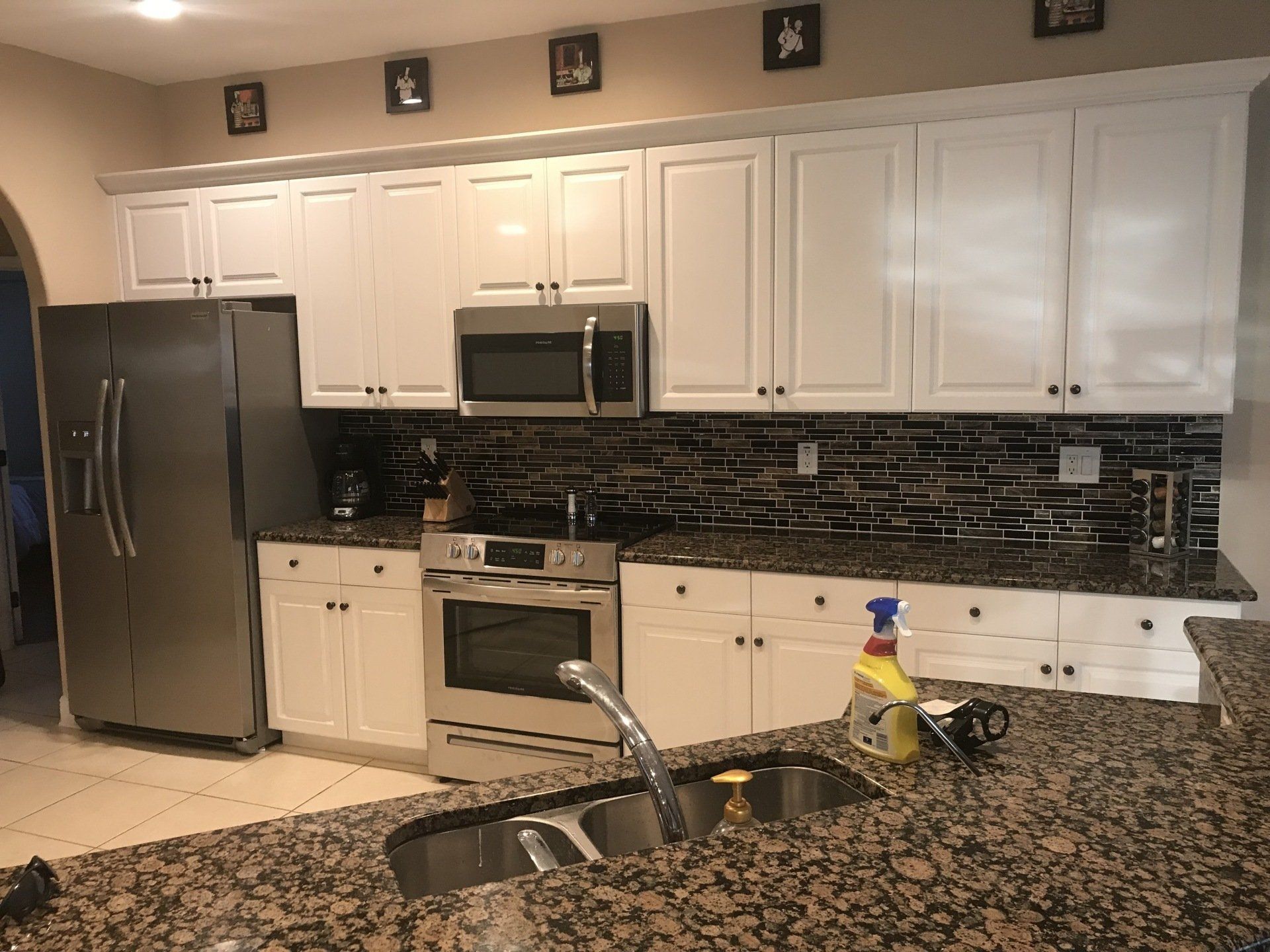 White kitchen cabinets with stainless steel appliances, granite countertops, and dark backsplash.