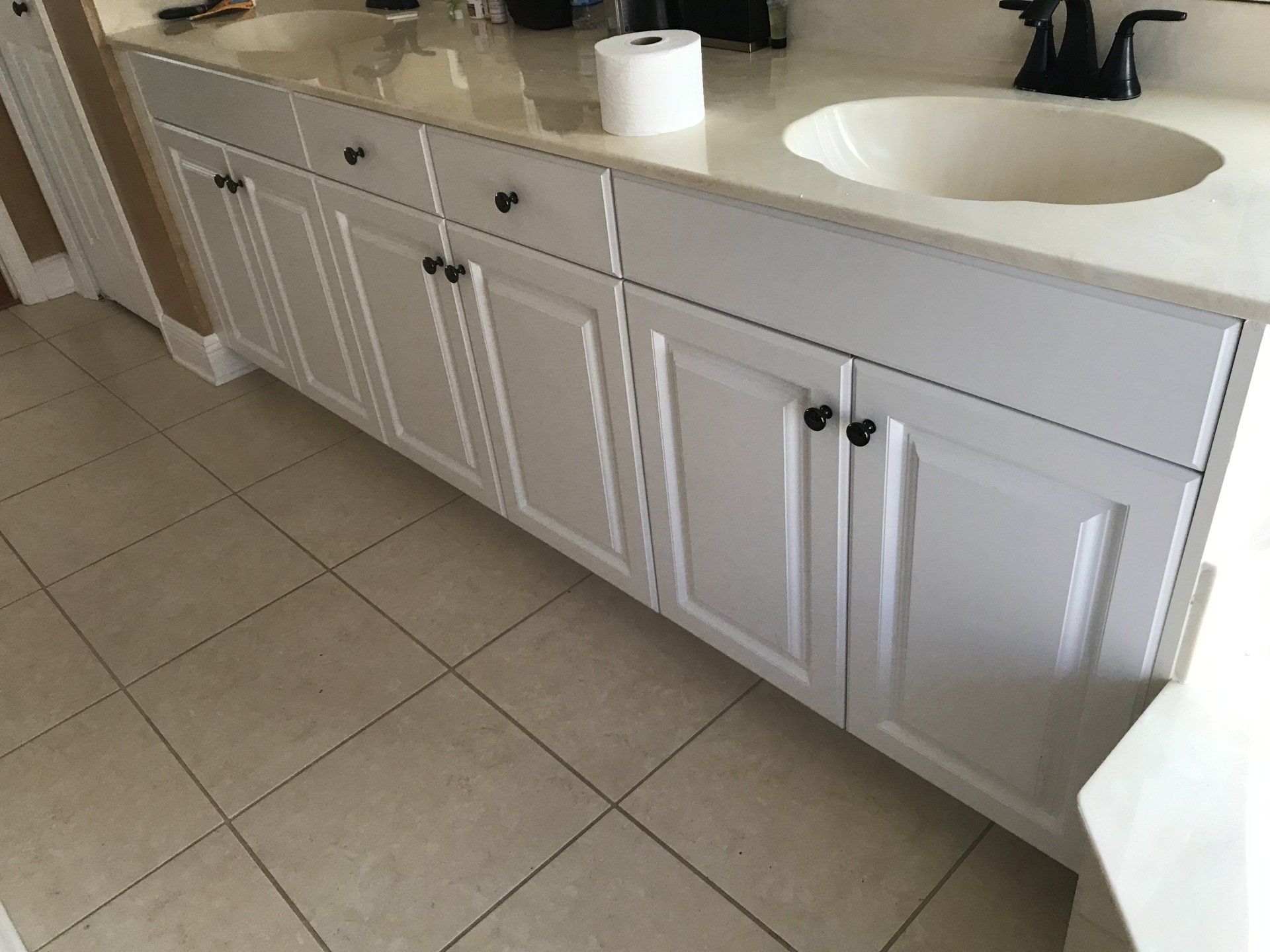 White bathroom vanity with black hardware, two sinks, and beige tile floor.