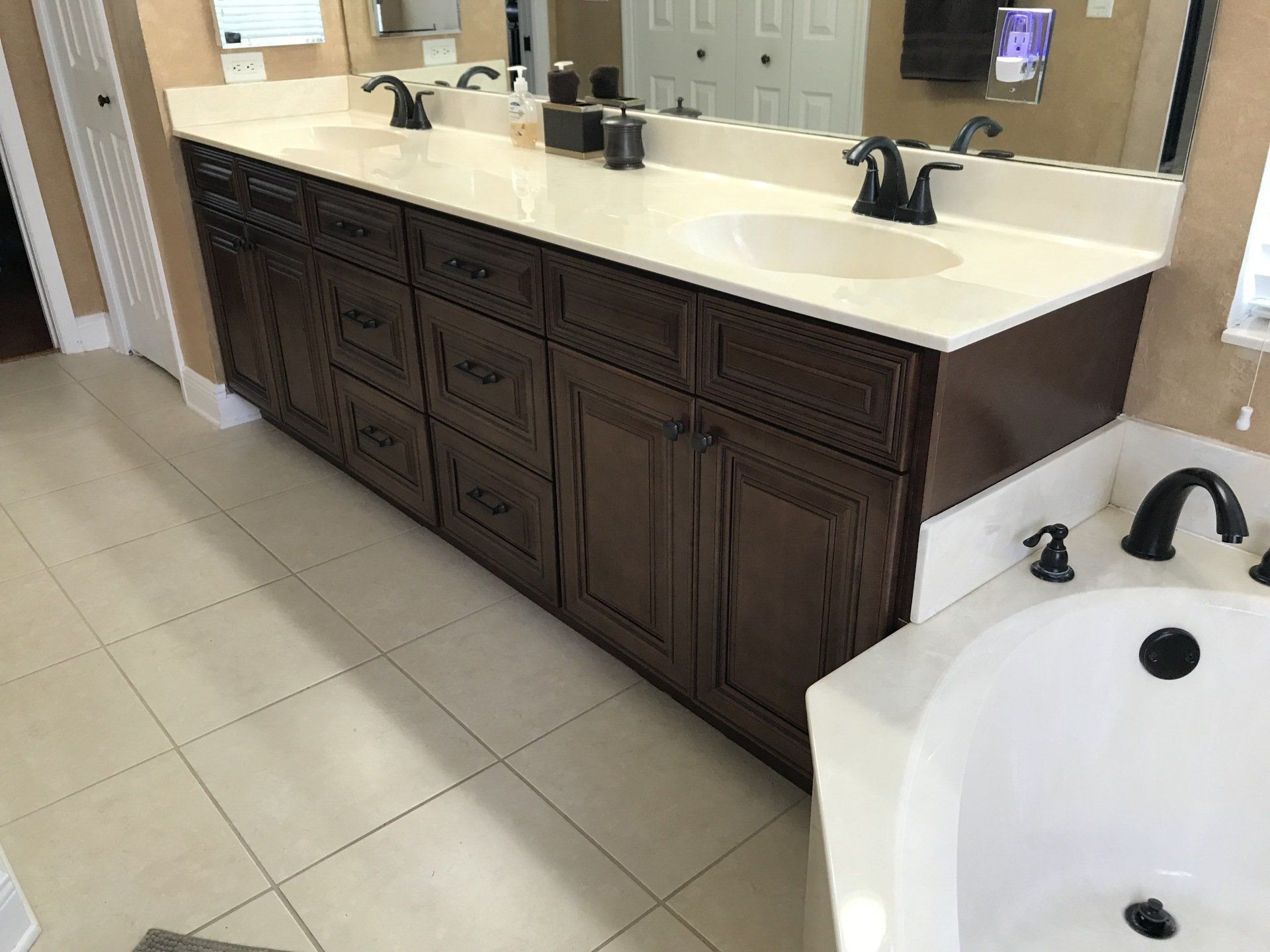 A long, dark brown bathroom vanity with a white countertop and two sinks, next to a white bathtub.