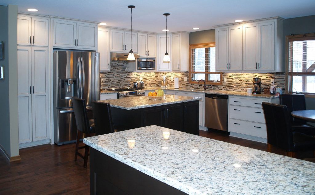 A modern kitchen with white cabinets, dark island, granite countertops, and stainless steel appliances.