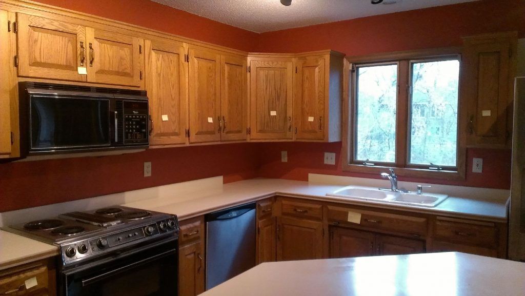 Kitchen with wooden cabinets, microwave, stove, white countertops, and window. Red walls.