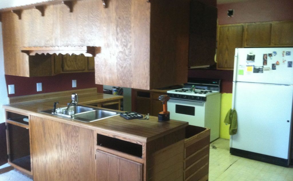Kitchen renovation in progress, showing wooden cabinets, island with sink, oven, and refrigerator.