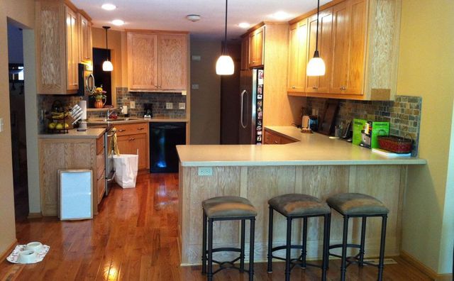 Kitchen with wood cabinets, island with stools, and hardwood floor.