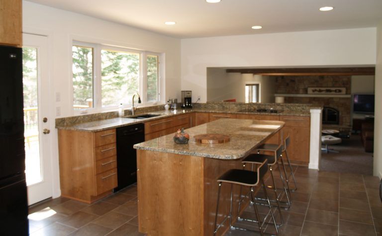 Kitchen with wood cabinets, granite countertops, island with bar stools, black appliances, and a view into a living room.