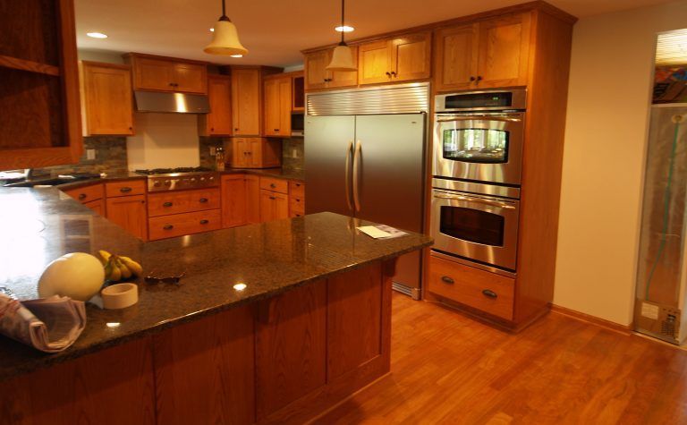 A kitchen with wooden cabinets, a stainless steel refrigerator and oven, and a dark granite island countertop.