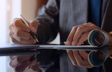 Hands writing on a document at a desk, with a blue folder nearby.