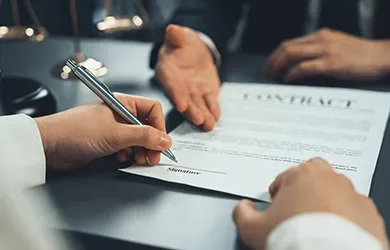 Hands signing a contract on a desk with a pen and papers.