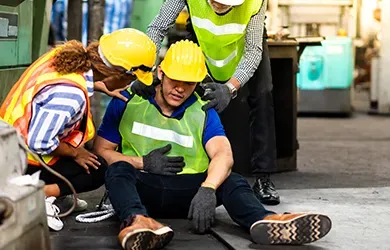 Worker in hard hat receiving first aid at a construction site, with coworkers assisting nearby