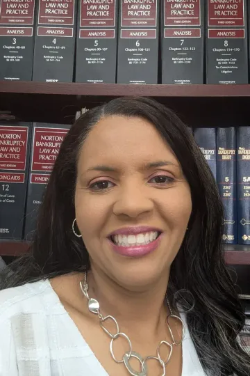 Smiling woman in white top and silver necklace in front of a bookshelf of legal books