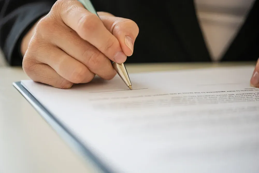 Hand holding a pen and signing a document on a desk