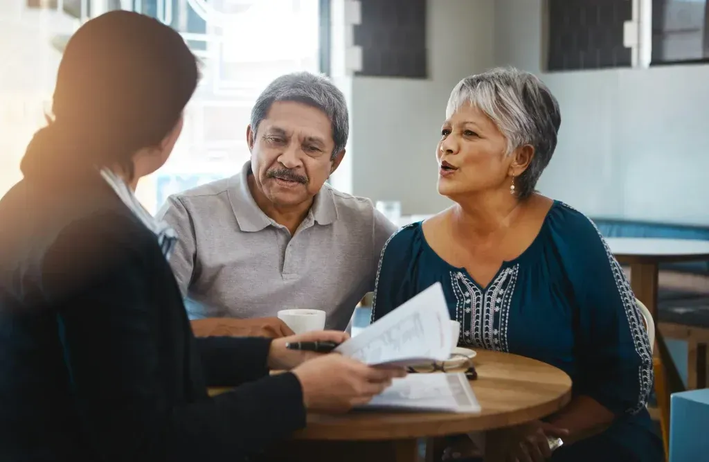 Three people discussing documents at a table in a bright office-like room
