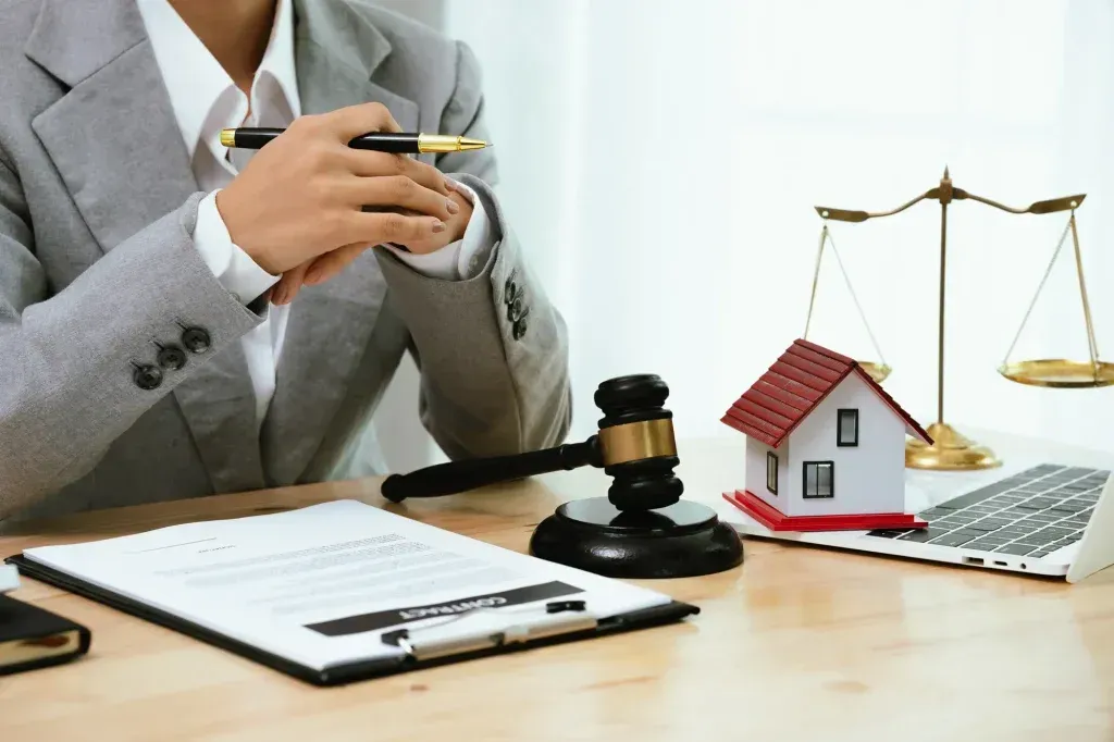 Lawyer at desk with gavel, house model, scales, and clipboard, suggesting property law or legal advice