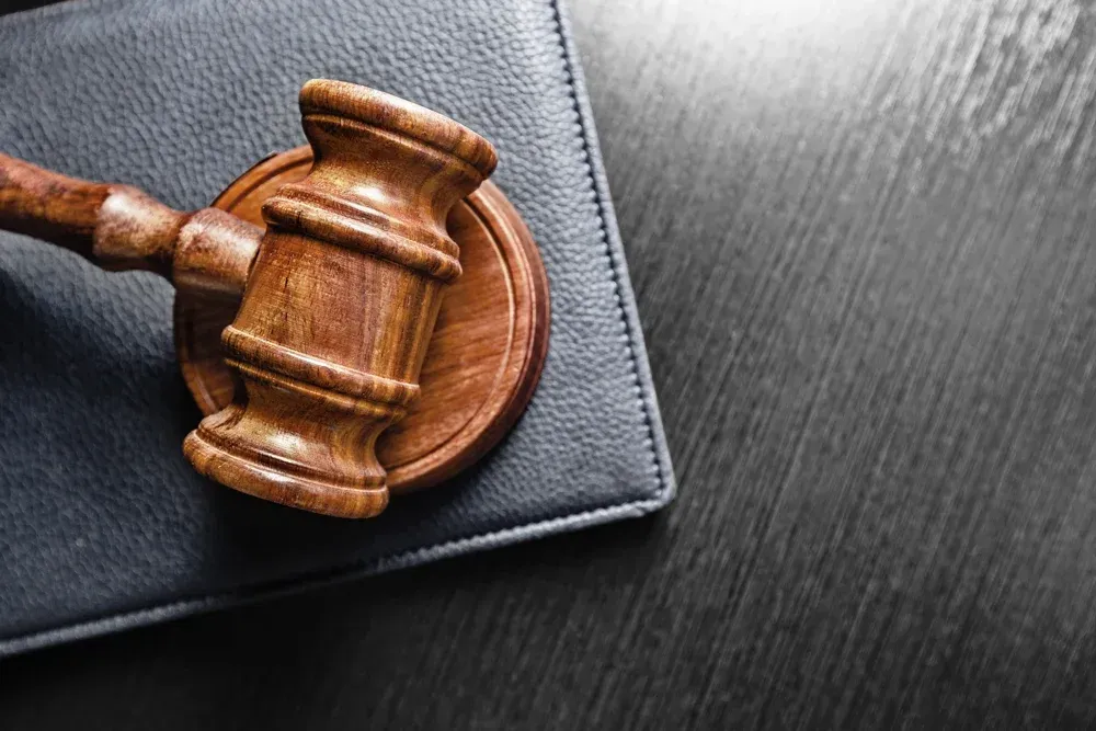 Wooden judge’s gavel resting on a black folder over a dark desk surface