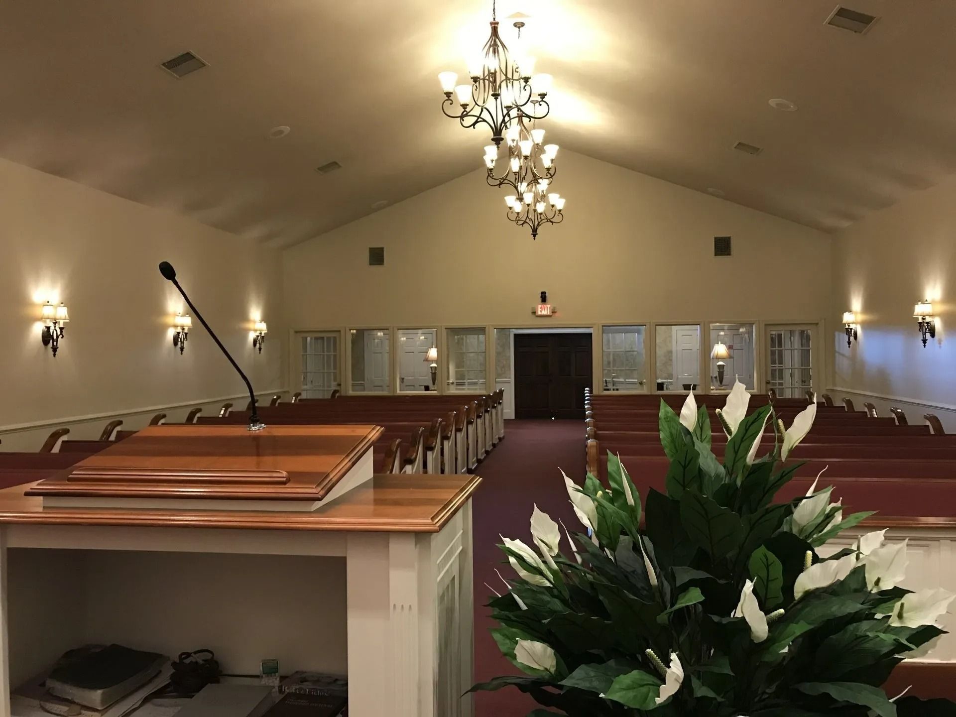 Interior of a church sanctuary with pews, a podium, and floral arrangement; chandelier and wall sconces illuminate the space.