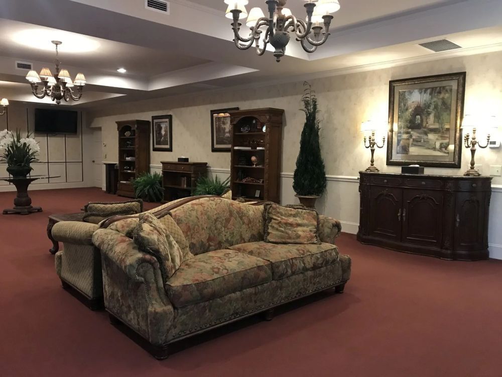 An elegant lounge area with a floral patterned sofa, antique furniture, and red carpet.